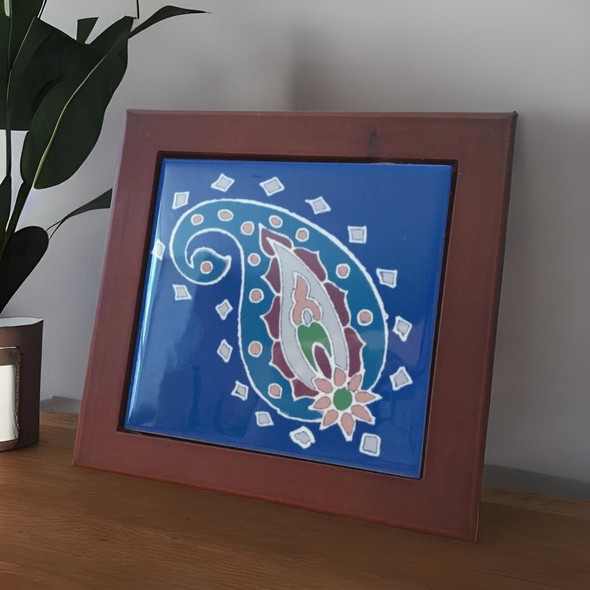 A professionally presented 10x10 cm printed ceramic tile featuring a vibrant blue background with a traditional Persian paisley (Boteh) motif set inside a sleek wooden frame against a clean white background.