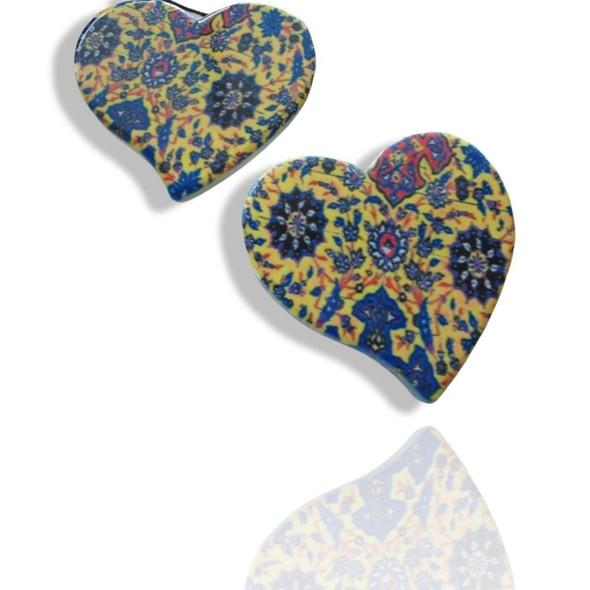 Two heart-shaped printed ceramic fridge magnets featuring a rich yellow background adorned with intricate blue, red, and dark traditional Persian floral and paisley patterns.