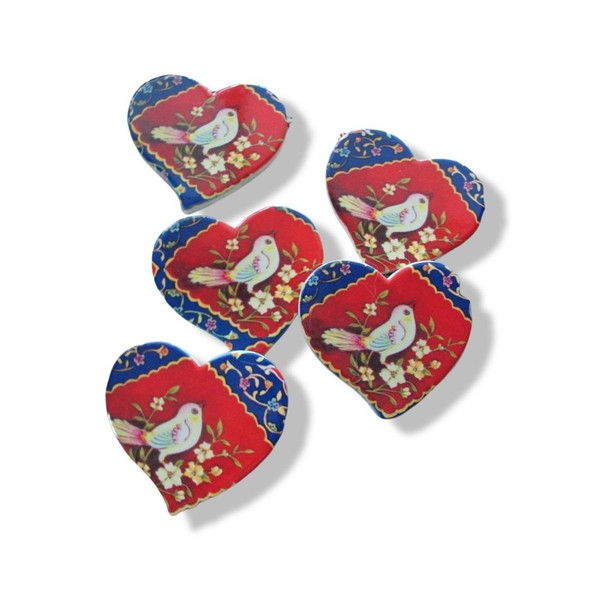 A collection of heart-shaped printed ceramic fridge magnets featuring a vibrant red center with a traditional white bird and floral branches, framed by a deep blue border.