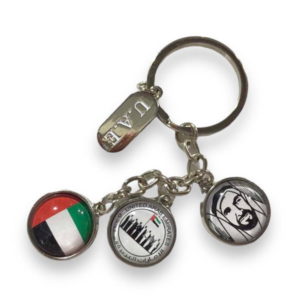 A professionally presented UAE national symbols charm keychain featuring multiple commemorative charms including the UAE flag, national emblem, leadership portrait, and 'U.A.E.' tag against a clean white background.