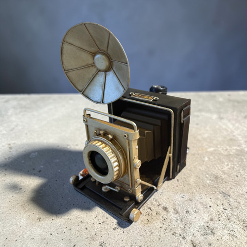 A handcrafted metal model of a vintage folding bellows SLR camera with an antique gold flash reflector.