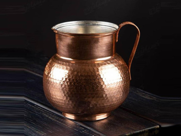 The 20 cm handmade copper jug shown as a sophisticated oriental decor centerpiece on a dark wooden table.