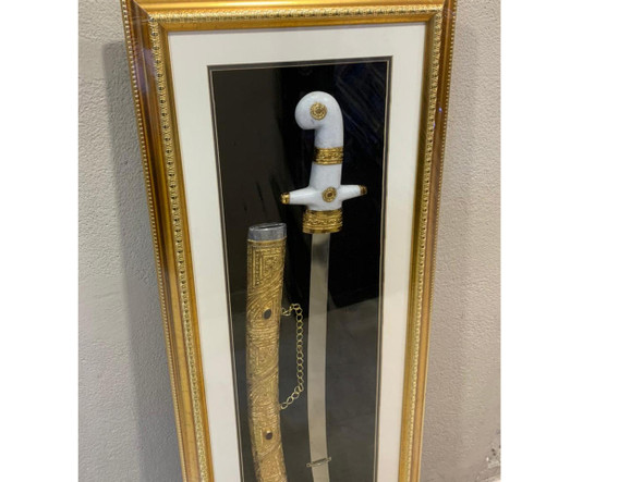 Detailed close-up of the ceremonial weapon inside the luxury frame, highlighting the intricate filigree engravings on the golden scabbard sleeve and the polished handle accents.
