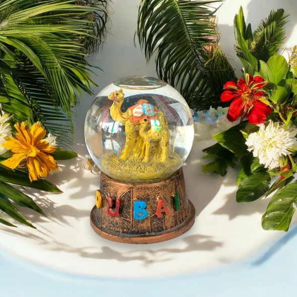 A professional product shot of the Dubai camel snow globe displayed on a dark wooden surface.Detail