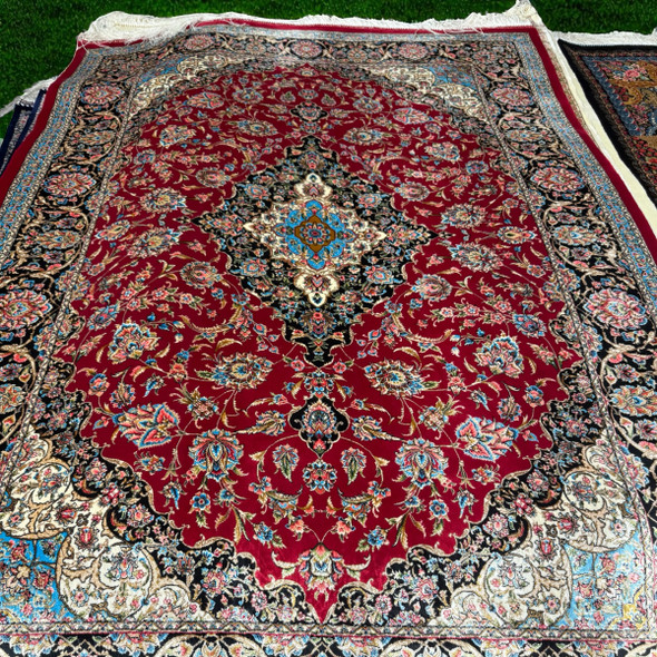 Close-up view of the fine silk weave, detailed floral motifs, and deep red and navy borders of the machinemade Persian carpet.
