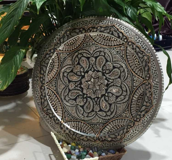 A professional product display shot of the 40 cm engraved copper tray positioned against a natural green foliage background.