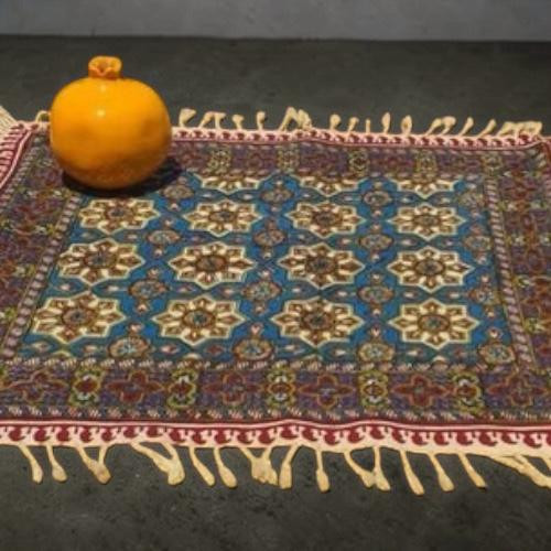 A 40x40 cm handmade Ghalamkari cotton place mat featuring a blue star pattern and red borders with hand-knotted fringe.