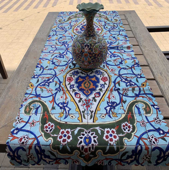 A 130x50 cm printed velvet table runner featuring a light blue background, dark green floral borders, and intricate scrollwork with a decorative vase on top.