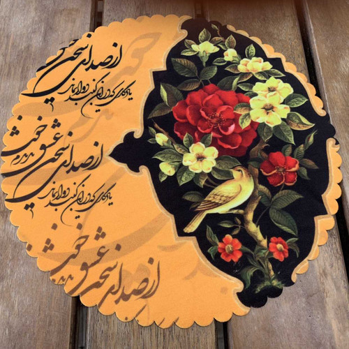 A 28 cm round velvet placemat on a wooden table featuring a hand-painted style bird and rose design alongside Persian calligraphy.