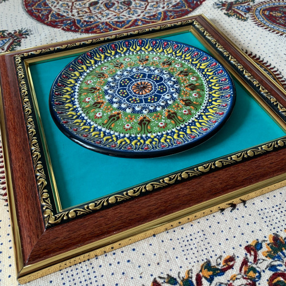 A traditional floral ceramic display plate beautifully enclosed in an exhibition frame hanging on an elegant living room wall.