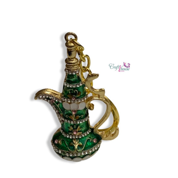 A miniature gold-toned metal Arabic coffee pot (Dallah) keychain against a neutral background.