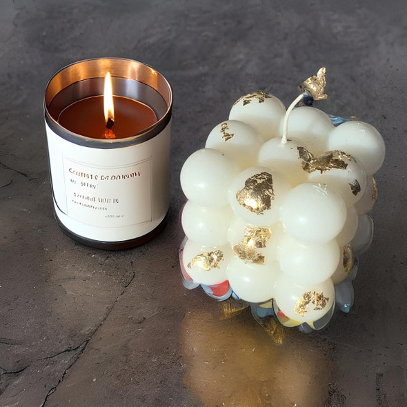 A detailed close-up highlighting the unique spherical bubble structure, smooth wax finish, and shimmering gold foil details of the decorative cube candle.