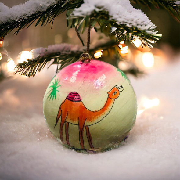 A hand-painted Christmas ornament ball featuring a silhouette of a camel and palm trees in a desert landscape.