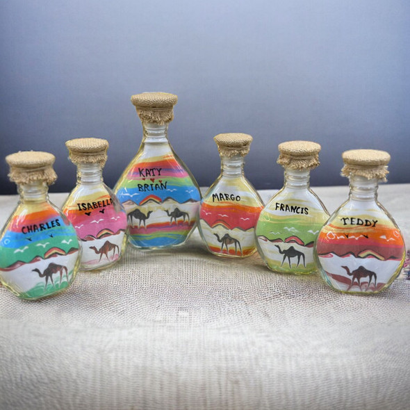 exhibition view of an authentic 13 cm glass sand art bottle featuring layered natural desert sands depicting a classic camel caravan under a customized name banner.