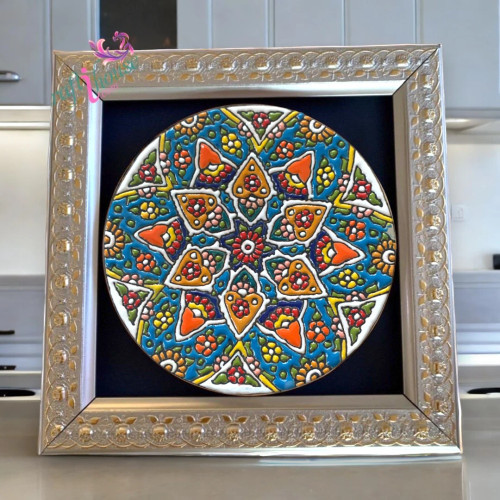 A framed Minakari ceramic plate hanging above a hotel room nightstand