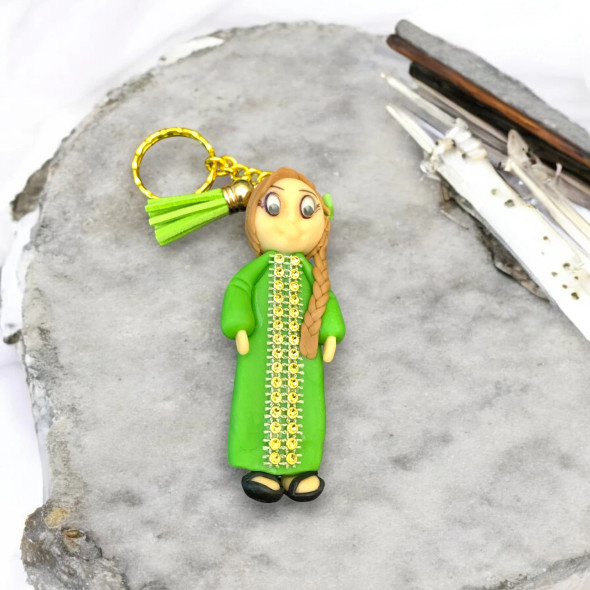 op-down exhibition view of a cute handmade polymer clay doll keychain dressed in traditional green Emirati attire, serving as a lovely gift or cultural travel souvenir.