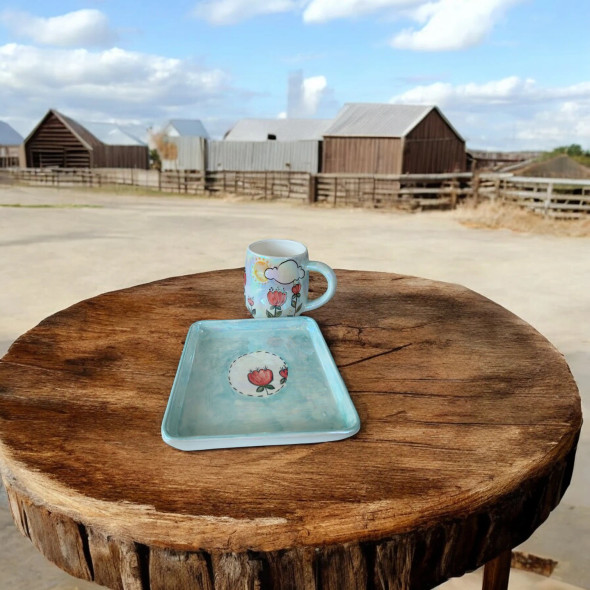 A professional product shot of the artistic autumn ceramic mug and matching square saucer displayed on a rustic round wooden stool.