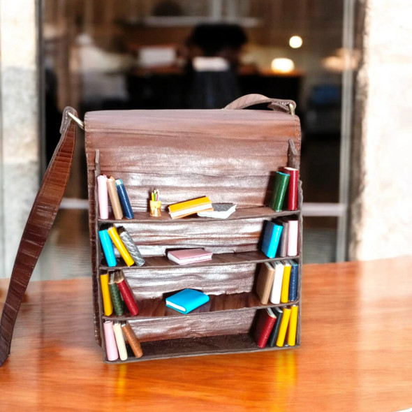 Close-up of the hand-finished 3D leather books on the bag, highlighting the different textures, colors, and spines of the "library
