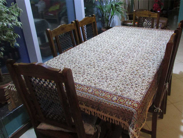 A rich floral woven tapestry tablecloth spread across a large wooden dining table