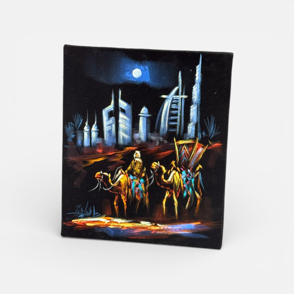 Close-up of the warm golden and orange oil paint details on black velvet, showing the textured 3D effect of the camel caravan.