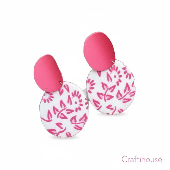 A pair of handcrafted white circular clay earrings featuring a vibrant pink botanical floral pattern and matching bold pink studs.