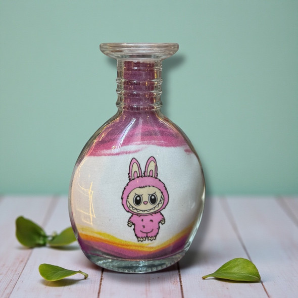 A 13 cm glass bottle filled with layered purple, white, and orange sand, featuring a cute pink bunny character in the center.