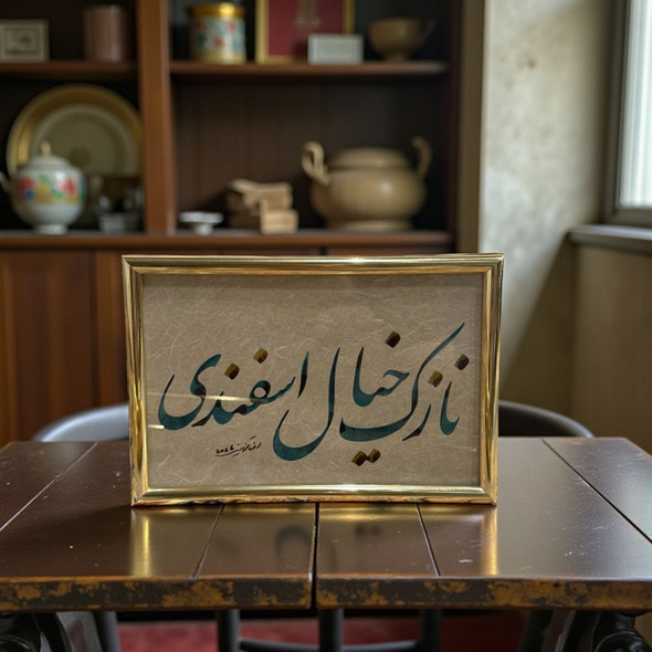 A framed Persian calligraphy piece featuring teal script and gold accents on textured paper, set in a polished gold-toned frame.