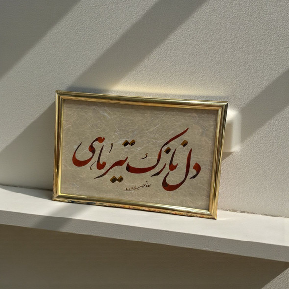 A framed Persian calligraphy piece featuring earth-toned script and gold accents on textured paper, presented in a polished gold-toned frame.