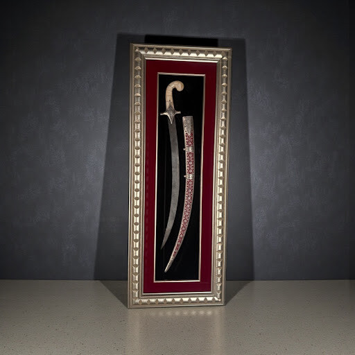 A premium vertical framed display of a curved Persian Shamshir sword and ornate red scabbard against a black velvet background.