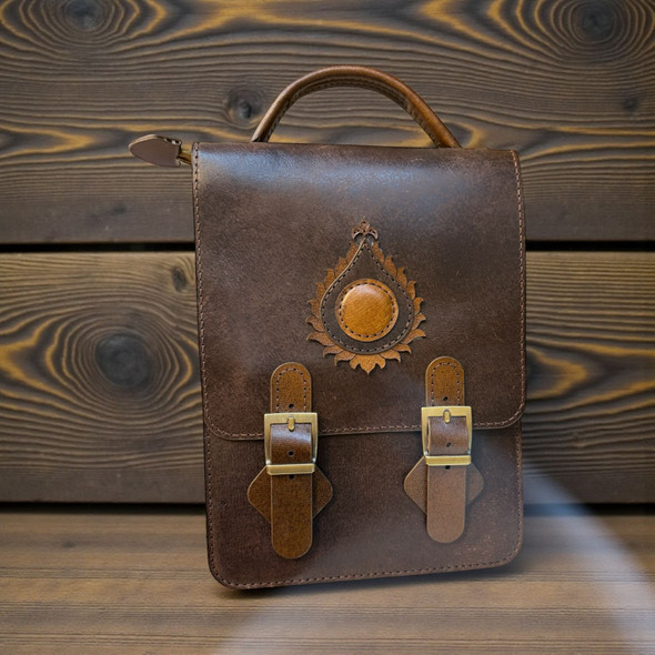 The front of the Nomad Executive Vertical Satchel in dark brown cow leather with a sunburst stitched emblem.