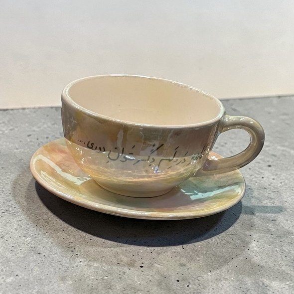 A professional product shot of the elegant hand-painted ceramic tea cup and matching saucer resting on a neutral gray backdrop.