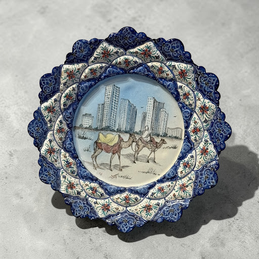 A 20 cm hand-painted Minakari copper plate featuring a camel caravan and city skyline pattern with a blue floral border.