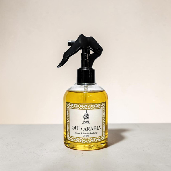 Front view of a 275ml bottle of Oud Arabia Home and Textile Perfume with a sleek black spray trigger mechanism, showcasing the rich golden liquid inside against a minimalist warm sand backdrop.