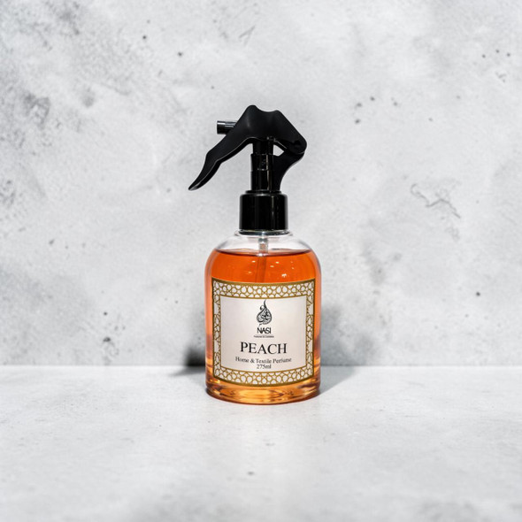 Front view of a 275ml bottle of Peach Home and Textile Perfume with a black spray trigger mechanism, displaying the vibrant amber fluid against a light textured stone backdrop.