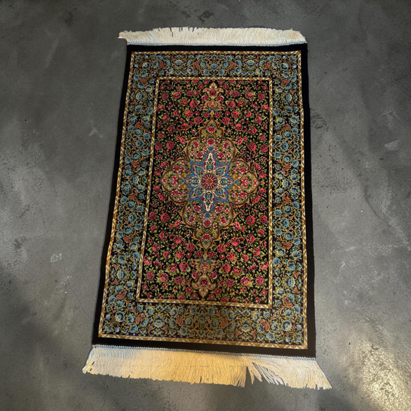 Product photo of the 50x80 cm , Machinemade carpet , Silk configuration, showcasing a rectangular machine-woven accent rug featuring a high-density traditional Persian design with a central eight-pointed floral medallion in light blue, gold, and white, surrounded by a dense field of small red and pink roses on a dark background, enclosed by an ornate light blue and gold border frame with a solid black outer edge and straight ivory-white fringes extending from the top and bottom widths, isolated on a clean white background.