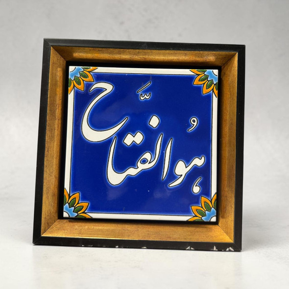 A 20x20 cm ceramic tile featuring the "Hovalfattah" calligraphy in white on a deep blue background, mounted in a 27x27 cm