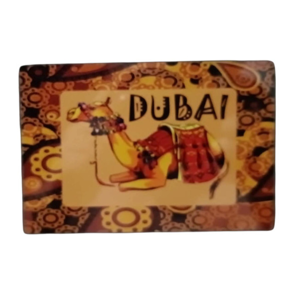 A rectangular 14x8 cm aluminum fridge magnet displaying a resting camel with traditional saddle adornments and the text "DUBAI," set against an ornate, warm-toned traditional background.