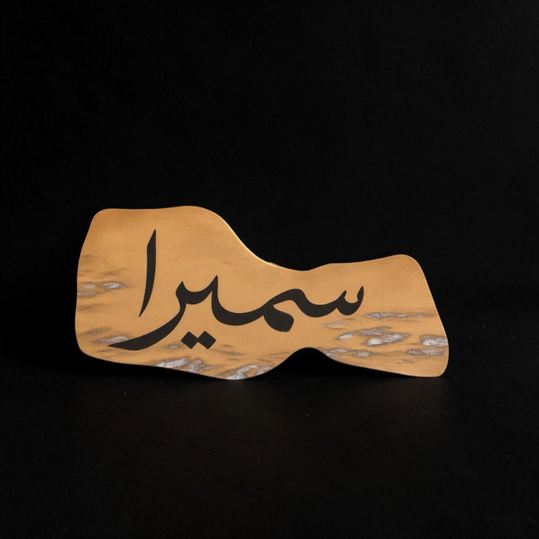 A personalized natural leather item featuring elegant Arabic name calligraphy, displayed neatly as a thoughtful spiritual gift on a warm wooden surface.