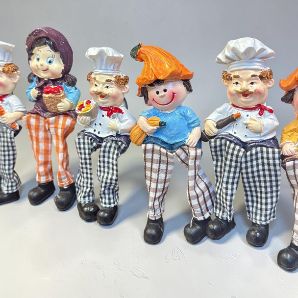 A lifestyle presentation showcasing the 6 assorted chef and village character magnets lined up together with dangling fabric legs.