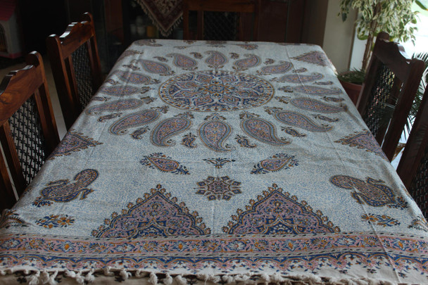 A round Persian Ghalamkari tablecloth with a blue and black central mandala on a circular wooden table