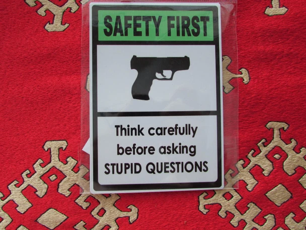 A vibrant 11x9 cm rectangular aluminium fridge magnet featuring a humorous 'Safety First' design with a handgun icon and the text 'Think carefully before asking STUPID QUESTIONS'.