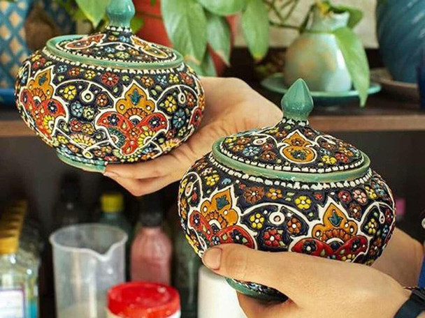 A handmade pottery sugar bowl with lid featuring vibrant, hand-painted enamel floral patterns on a dark blue clay base.