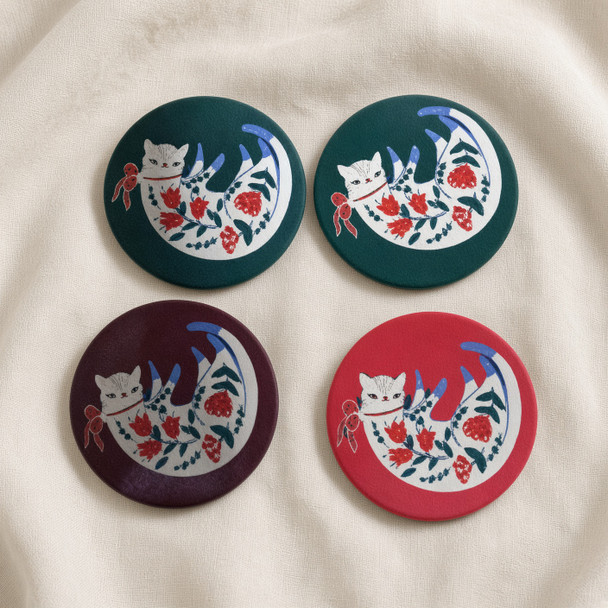 A professionally presented 4-piece set of round printed ceramic coasters featuring a sleeping folk-art cat adorned with red floral motifs against teal green, burgundy, and coral red background variations.