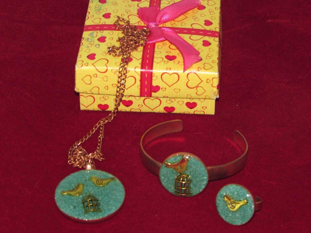 A 3-piece handmade copper jewelry set featuring a bird and cage motif necklace, bracelet, and ring with a yellow heart-patterned gift box.