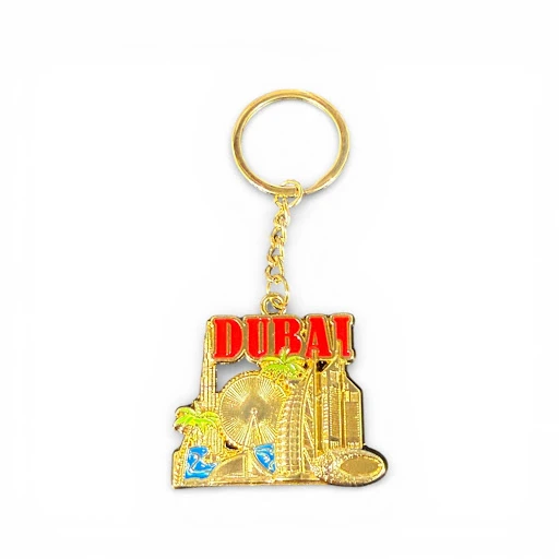 A premium gold-toned keychain featuring the Dubai skyline with red "DUBAI" text and blue enamel accents.