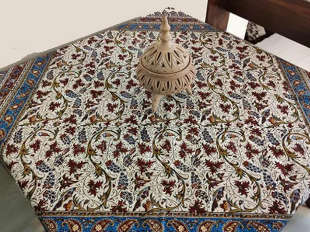 A professional display of the 120x120 cm cotton Ghalamkari textile used as an elegant decorative tablecloth in a warm home setting.