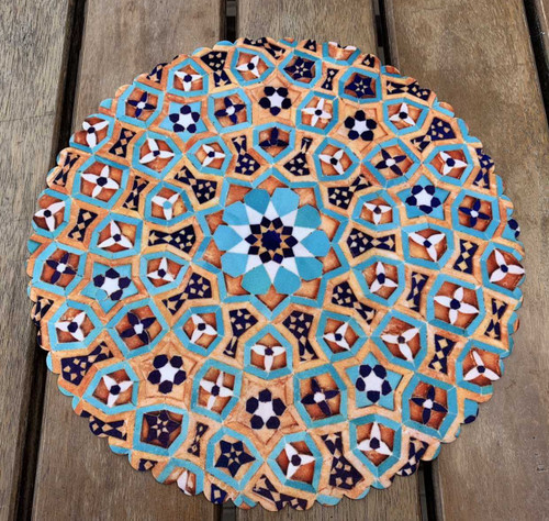 A 28 cm round velvet placemat featuring a complex blue and orange geometric star pattern on a wooden table.