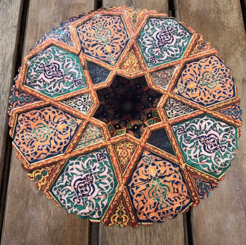 A 28 cm round velvet placemat on a wooden table featuring a complex multi-colored star pattern inspired by Persian architectural tiles.