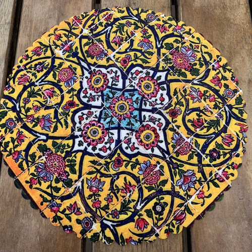 A 28 cm round velvet placemat with a vibrant yellow floral tile-inspired pattern on a rustic wood background.