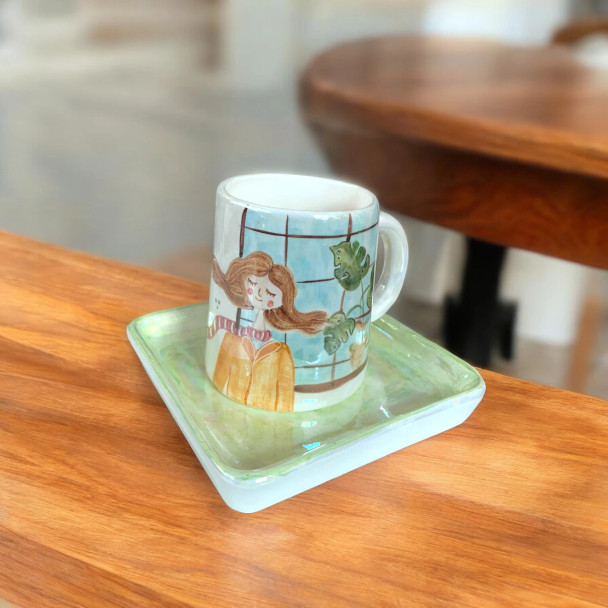 A beautiful close-up of a hand-painted ceramic mug and tray set with cute artistic girl detailing.